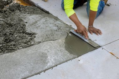 İnşaat işçisi, yeni dökülmüş beton kaldırımları düzleştirmek için çelik mala tutuyor.