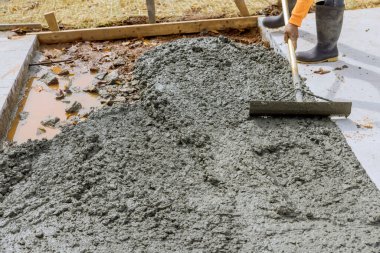 İşçi çelik kürek tutuyor inşaat alanında yeni dökülmüş beton kaldırımı düzleştiriyor.