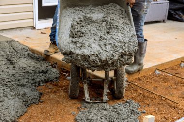 İşçiler evin yakınına ıslak beton dökerek kaldırım yolu açmak için el arabası ıslak çimento kullanıyorlar.