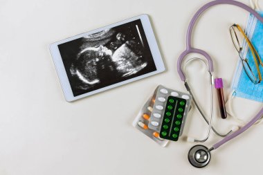 Tıp bürosundaki doktor, doğmamış çocuğun korunması için reçete yazan hamile kadının ultrasonunu inceliyor.