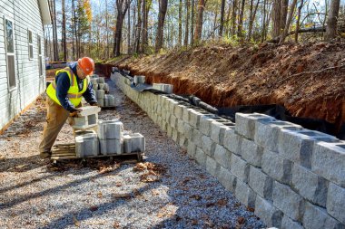 Müteahhit, kısmen yeni istinat duvarı inşaatı üzerine inşa edilen beton blok duvarı yerleştirirken görüldü.