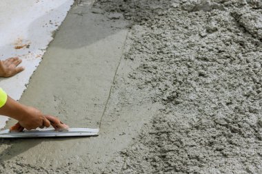 İnşaat işçisi çelik malayı yeni dökülmüş beton kaldırımı düzleştirmek için tutuyor.