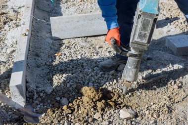 İnşaat yolu inşaatının bir parçası olarak kaya matkabını kullanan işçiler beton yüzeyleri kazıyor ve kazıyor.