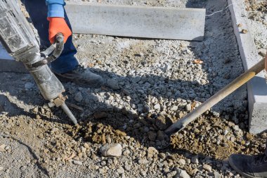 İnşaat işçileri yol kenarındaki beton yüzeyi kazmak için matkap kullanıyorlar.