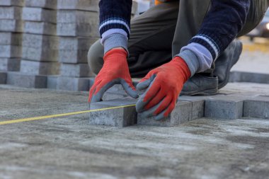 Evin avlusunda avlu oluşturmak için kumların temeline gri beton levhalar döşeyen bir usta var..