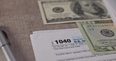 An American dollar bill, pen calculator and U.S. 1040 individual tax form are placed on desk of American citizen.