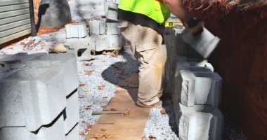 There was worker on construction site installing concrete block for retaining wall near new house that was being built
