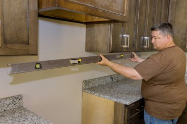 During installation of new kitchen cabinets worker hangs level to ensure that cabinets are level