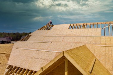 An unfinished house is being reroofed by roofer who is working on installation of plywood roof