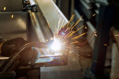 Worker is welding with semi-automatic argon gas shielded welding machine on metal that has sparkles in it