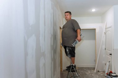 In course of renovating room, worker plastered plasterboard and constructed drywall walls.