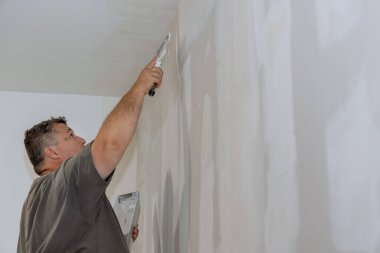 Worker plastered plasterboard wall during renovation of room in which drywall wall is being constructed.