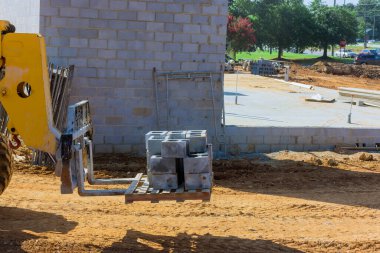 Cement blocks are moved by boom forklift truck to place where wall of house is be installed