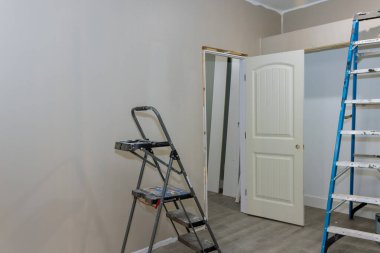 Wall painted in empty room with painting equipment and stepladder next room that is empty