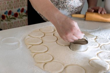 Using rolling pin to cut raw homemade dough into round pieces on bakery table making homemade donuts