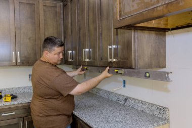 Installing new kitchen cabinets furniture set by worker who is using level for leveling