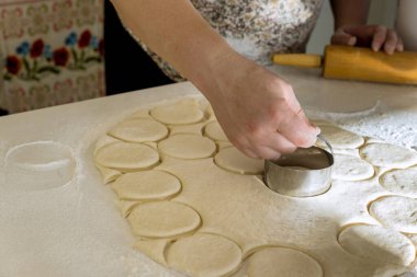 Raw homemade dough for donuts that has been cut into round pieces with rolling pin on bakery work table