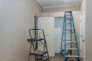 In an empty room, one can see painted wall with painting equipment and stepladder close to it