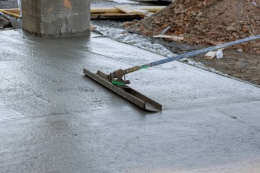 Using long trowels worker in construction site leveled wet cement sidewalk that was being poured with concrete.