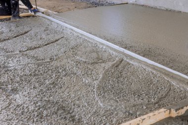 Construction worker leveled an pouring concrete using long trowels on a wet cement sidewalk.