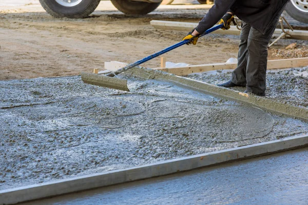An employee of construction company leveled wet concrete sidewalk with use long trowels after pouring concrete.