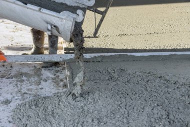 On building site concrete mixing truck is pouring concrete for pavement surrounding newly constructed home