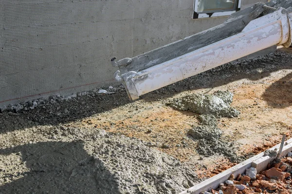 Concrete mixing truck pours concrete onto building site surrounding newly constructed home so that it can make pavement