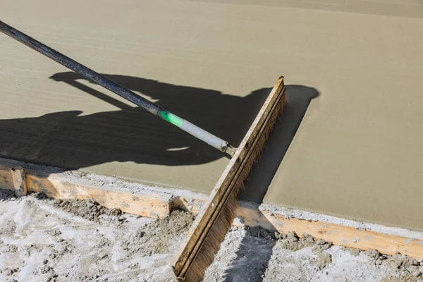 Construction laborer use broom to brush fresh wet concrete causing groove texture pattern surface