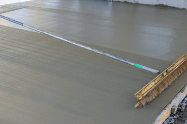 Construction workers use broom to brush freshly wet concrete on surface resulting in formation of groove texture patterns