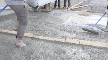 Construction worker leveled an pouring concrete using long trowels on a wet cement sidewalk.