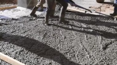 Concrete is being poured from concrete mixing truck around new house to create pavement for it