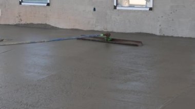 After pouring concrete over wet concrete surface worker plasters floor with trowel using