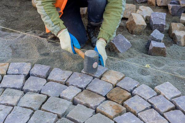 Worker were using industrial cobblestones to pave sidewalk with granite stones.