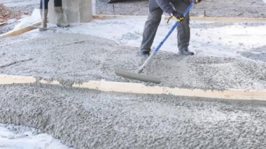 İnşaat şirketinin bir çalışanı beton döktükten sonra uzun malalar kullanarak ıslak beton kaldırımı dümdüz etti..