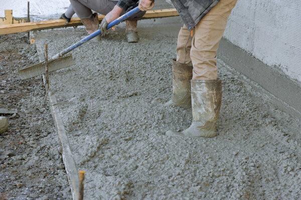После заливки бетона сотрудник использовал длинные лопатки, чтобы выровнять тротуар.