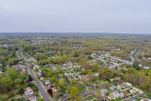 An aerial view of small American town residential complex district with houses and roads surrounded by spring trees can be seen from above.