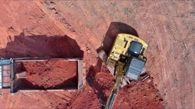 Çöp kamyonu inşaat alanındaki bir kazıcıya toprak yüklüyor.