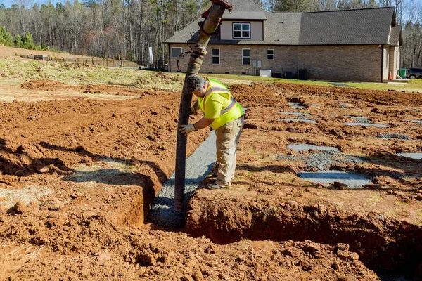 Worker pours concrete for foundation of building while controlling automatic pump to pour cement concrete