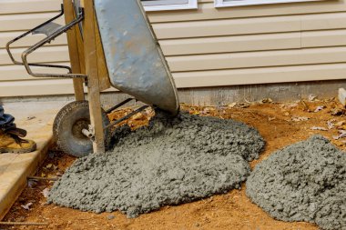 İnşaat işçisi, gelecekte kullanılacak beton kaldırımlar için el arabasından çimento döküyor.