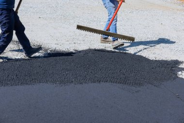 Yol kaldırımlarında çalışan işçiler asfalt döşeyip siyah çakılları kürekliyor ve kaldırıma hazırlıyorlar.