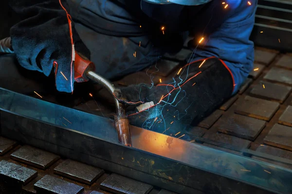 In this workplace worker is welding steel at work sparks are lighting smoke throughout factory as he works