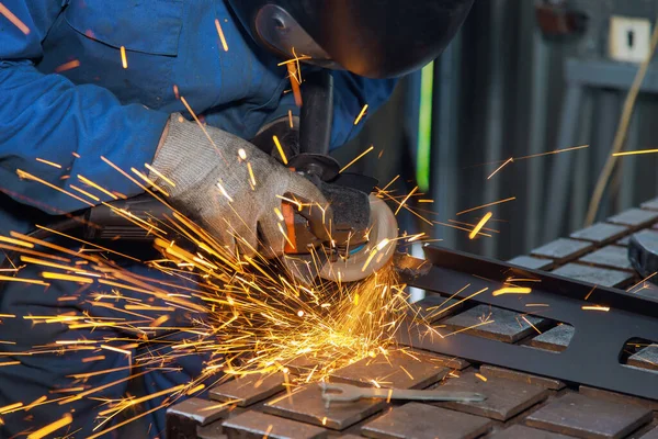 An industrial metal work site has master who grinds metal with grinder sparking as he works on metal