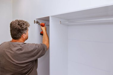 Marangoz, odaya yerleştirilmesi gereken mobilya dolabını monte etmeye çalışıyor.