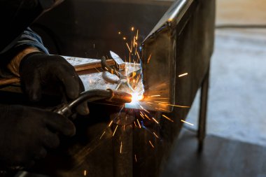 Ağır sanayide deneyimli bir işçi koruyucu maske takıyor ve fabrikada argon ile kaynak yapıyor.