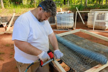 İşçi çivi tabancasıyla metal ağı ahşap çerçeveye çiviliyor