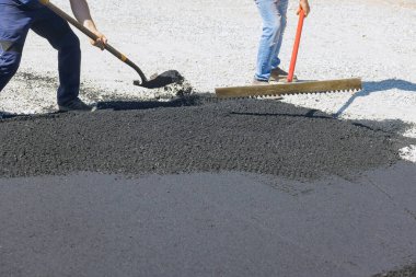 Yol kaldırımlarına asfalt döşeyen çalışmalara asfalt döşemek amacıyla siyah çakıl küreyen adamlar da eşlik ediyor.