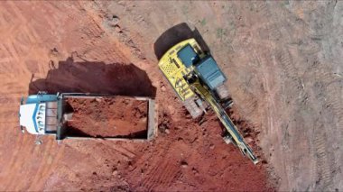 Bir kazıcı inşaat alanındaki ağır kamyona toprak yüklüyor.