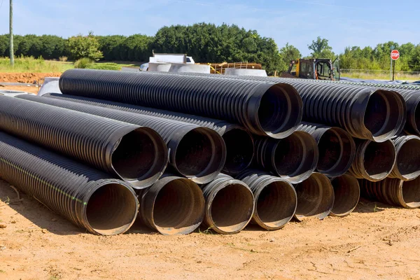 Büyük siyah plastikten yapılmış sanayi kanalizasyon boruları düzgünce istiflenmiş ve inşaat sahasına yerleştirilmeye hazır..