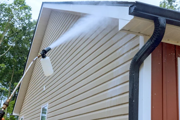 Water soap cleaner is sprayed onto siding houses by service worker, employing high pressure nozzles.