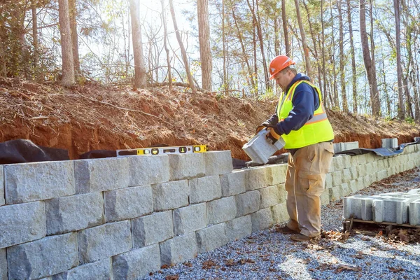 Yeni inşaat işçisi geliştirirken istinat duvarı inşa etmek için beton blokları kullanır.